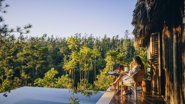 Eine Person sitzt am Pool mit Blick auf einen Wald.