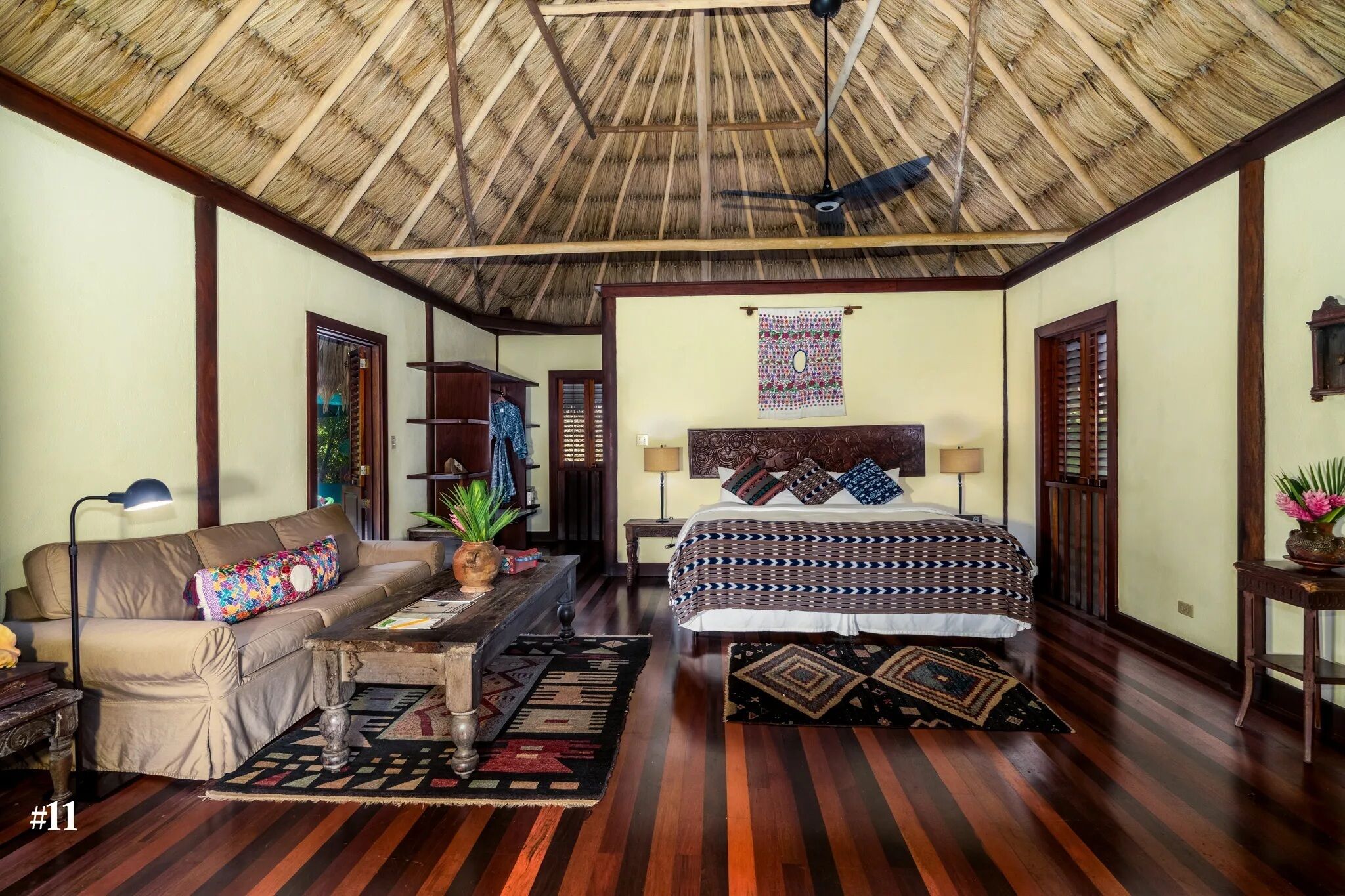 A room with a bed, a sofa, a small table, and a ceiling fan.