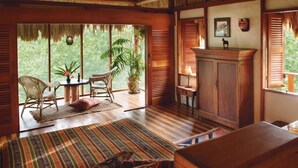 Ein Zimmer mit großem Fenster, Korbmöbeln, einem Holzschrank und einem Streifen Teppich.