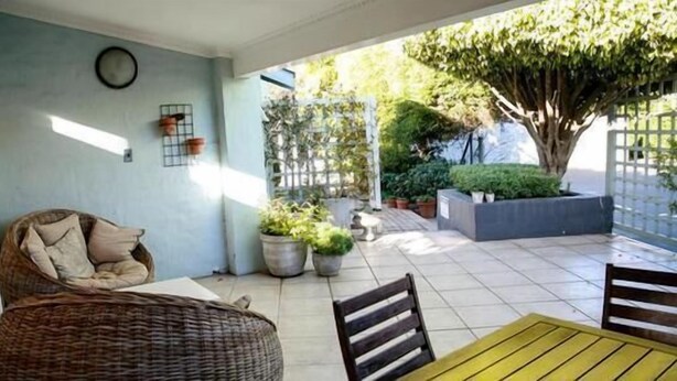 A patio area with a wicker sofa, a yellow table, and potted plants.