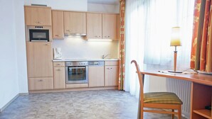 A compact kitchen with wooden cabinets, a built-in oven, and a dining area with a chair and table.
