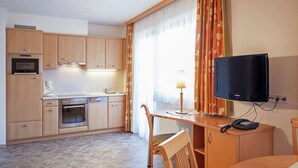 A compact hotel room with a kitchenette, a television, a desk, and a chair.