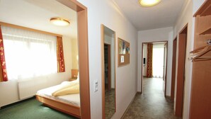 A hotel room with a bed, a mirror, a radiator, and a hallway leading to another room.