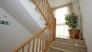A staircase with wooden railings, a green emergency exit sign, a potted plant, and a window with curtains.