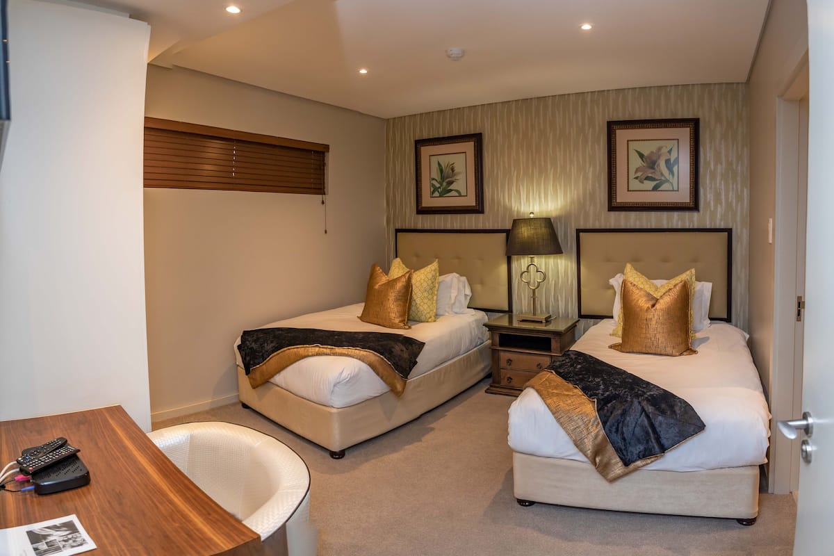 A hotel room with two beds, a desk, a chair, and a lamp.