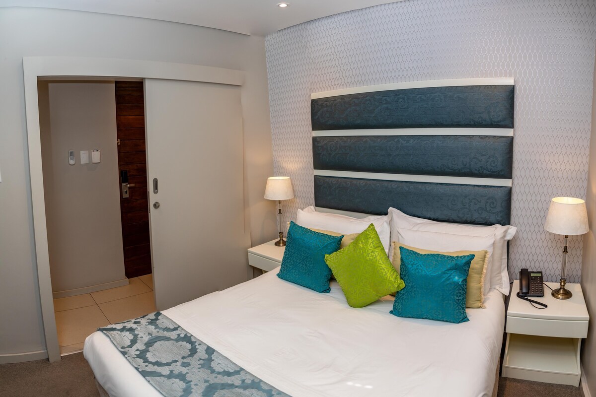 A modern hotel room with a large bed, two bedside tables with lamps, and a patterned headboard.