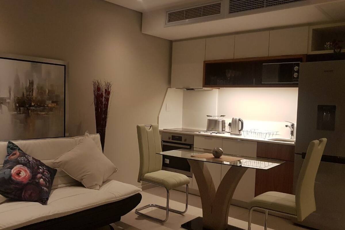 A modern kitchen with a dining area, a sofa with cushions, and a cityscape painting on the wall.