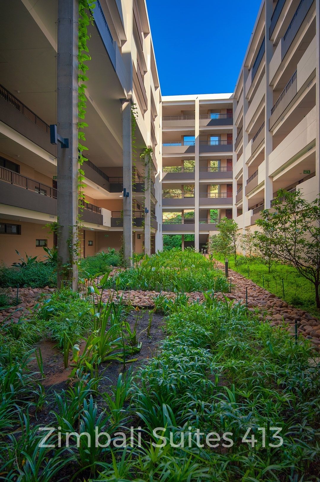 A multi-story building with balconies and a garden area in the foreground.