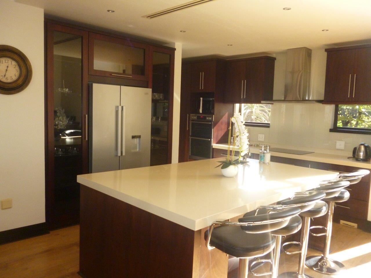 A modern kitchen with a large island, bar stools, stainless steel appliances, and dark wooden cabinets.