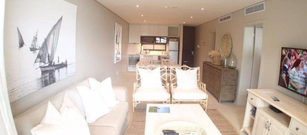 A living room with a sofa, two armchairs, a coffee table, a TV, and a kitchen in the background.