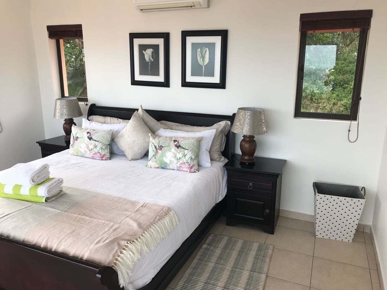 A neatly arranged bedroom with a bed, bedside tables, a lamp, and a trash bin.