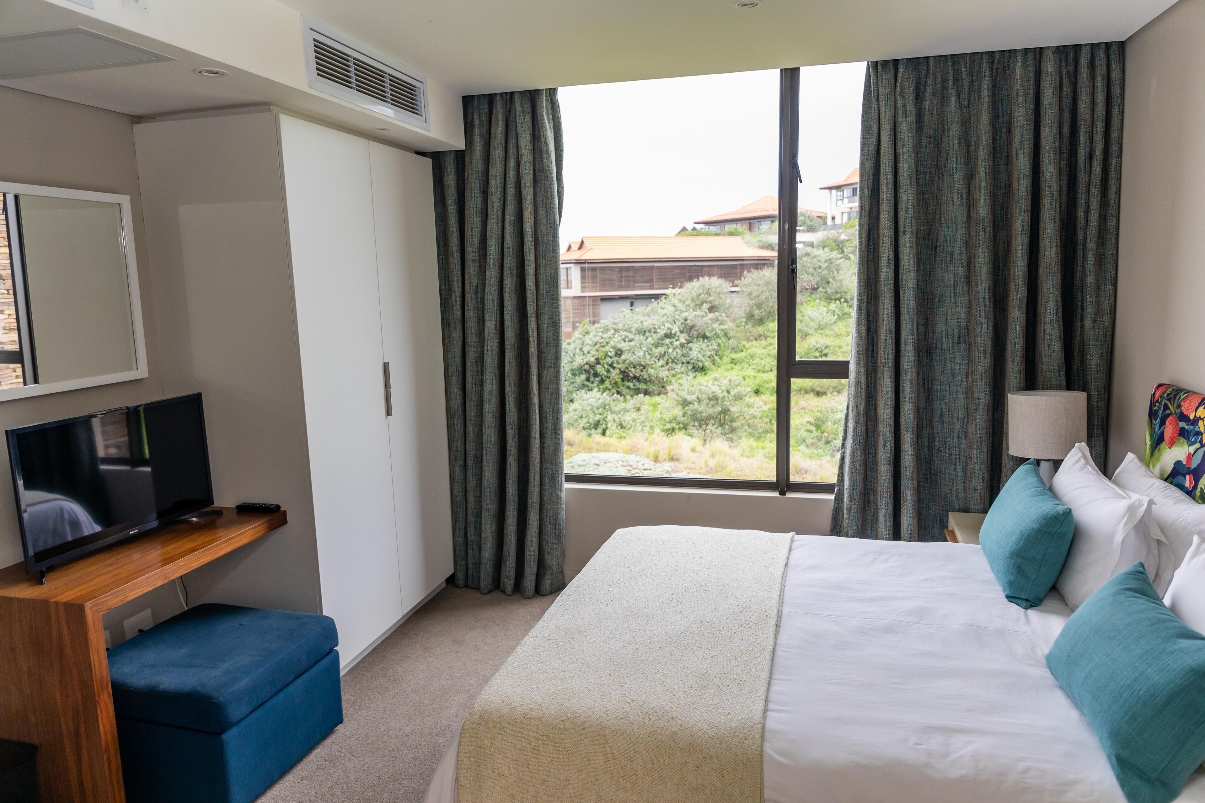 A hotel room with a bed, a TV, a desk, and a window with curtains.