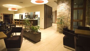 A modern hotel lobby with a central seating area, a stone accent wall, and a kitchen visible in the background. - Hotel Mar de Plata (Sarria)