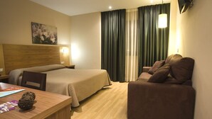 A hotel room with a wooden headboard bed, a sofa, a desk with a lamp, and a painting on the wall. - Hotel Mar de Plata (Sarria)
