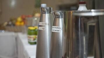 Des distributeurs d’eau en acier inoxydable, portant l’inscription « Agua Caliente Hot Water », sont placés sur une table.