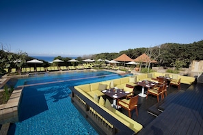 A poolside area with lounge chairs, umbrellas, and a dining setup overlooking a body of water. - Zimbali beach estate  (Ballito)