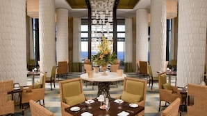 A spacious dining area with high ceilings, large windows, and a central round table surrounded by wicker chairs. - Zimbali beach estate  (Ballito)