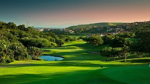 A golf course with a pond, trees, and houses in the background. - Zimbali beach estate  (Ballito)