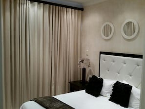 A hotel room with a large bed, a nightstand, a lamp, and a window with curtains. - Zimbali beach estate  (Ballito)