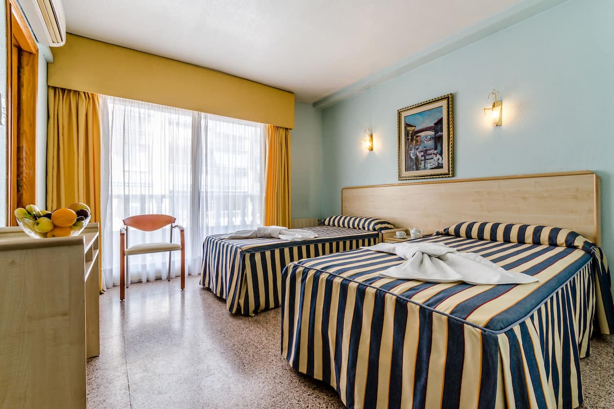 A hotel room with two beds, a wooden desk, a chair, and a fruit bowl.