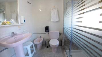 Baño con lavamanos, bidé, inodoro y una toalla colgada en la pared.