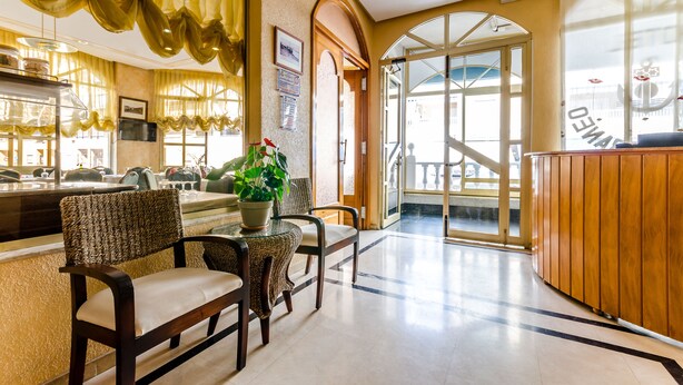 A hotel lobby with a reception desk, seating area, and a large window. - Hotel Mediterraneo (Guardamar del Segura)