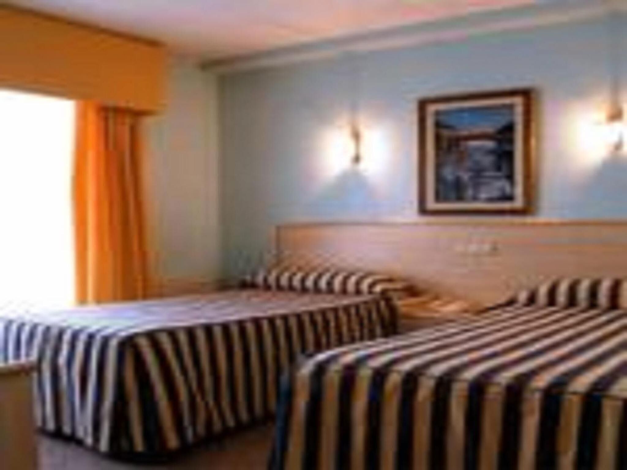 Een hotelkamer met twee bedden, gestreepte beddengoed, een ingelijst kunstwerk aan de muur en een raam met gordijnen.