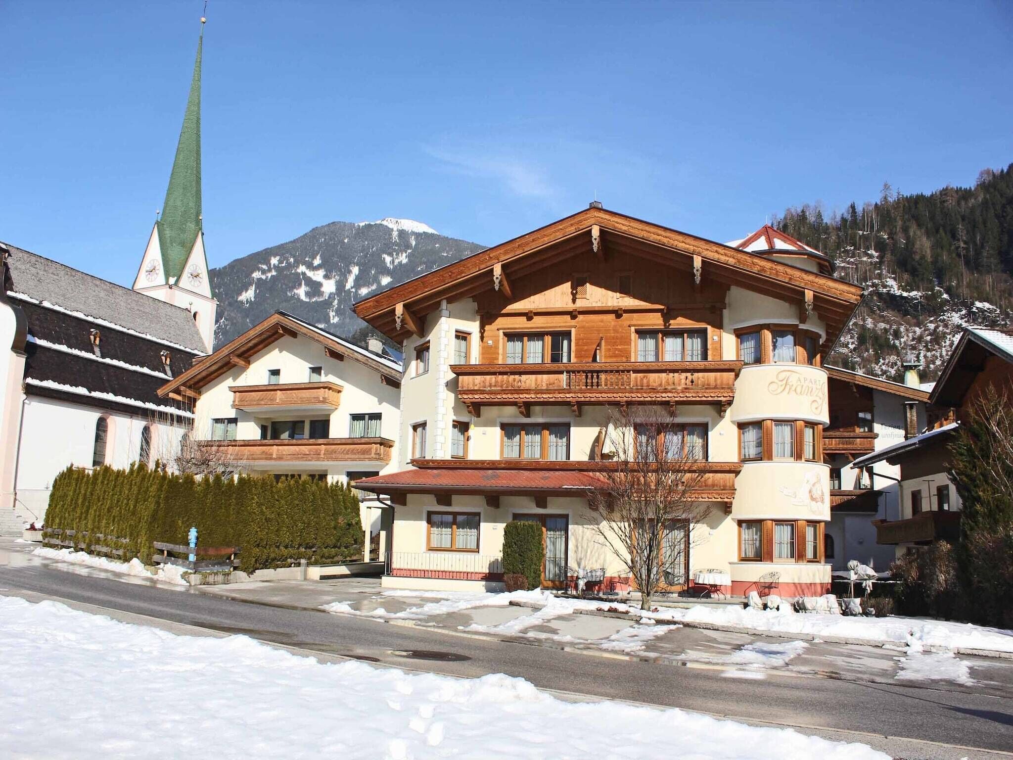 A multi-story hotel with a traditional Alpine architectural style, featuring wooden balconies and a mountain backdrop.
