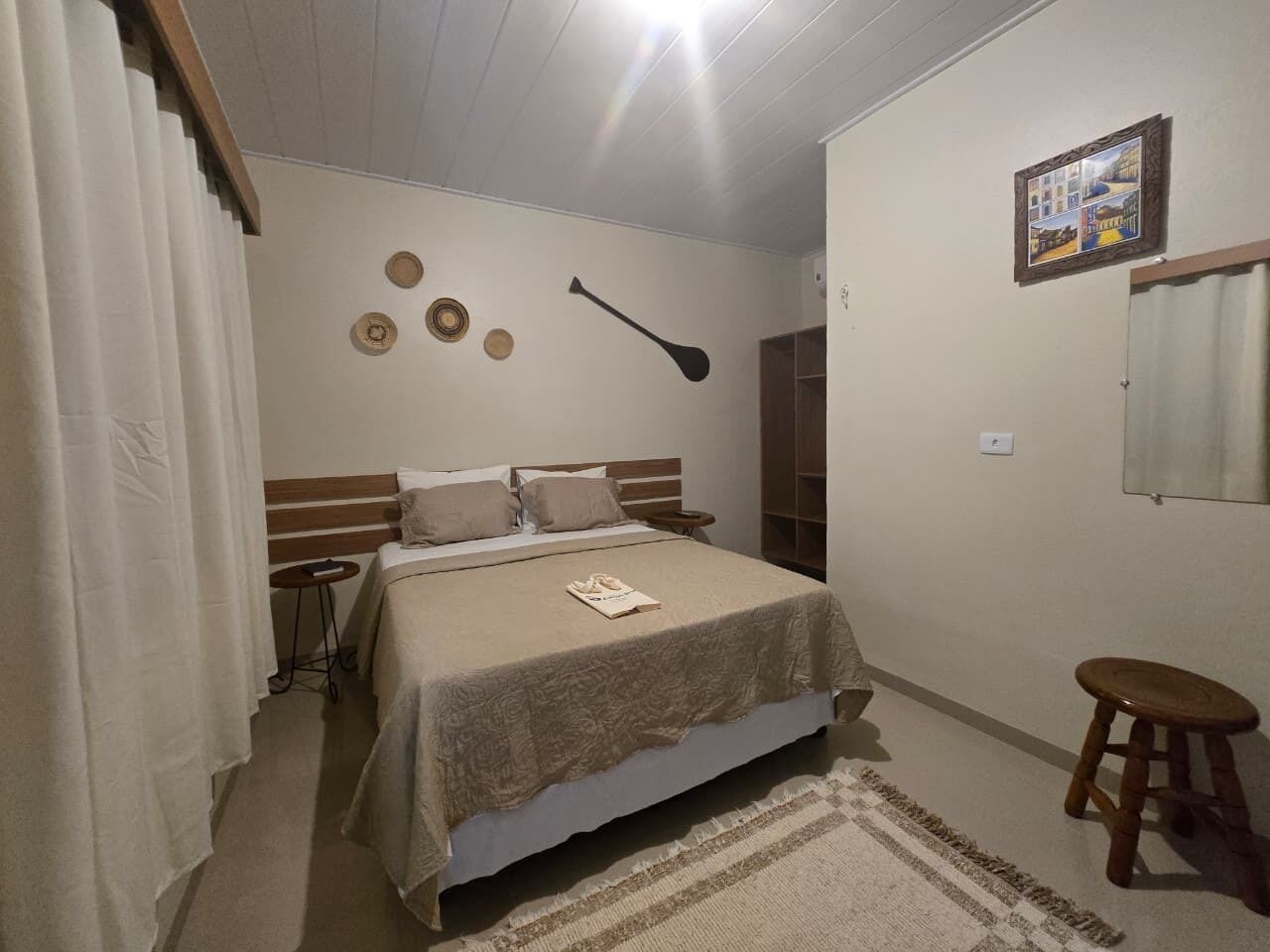 Un dormitorio con cama, mesita de noche, lámpara colgante, un taburete pequeño y estante de pared.