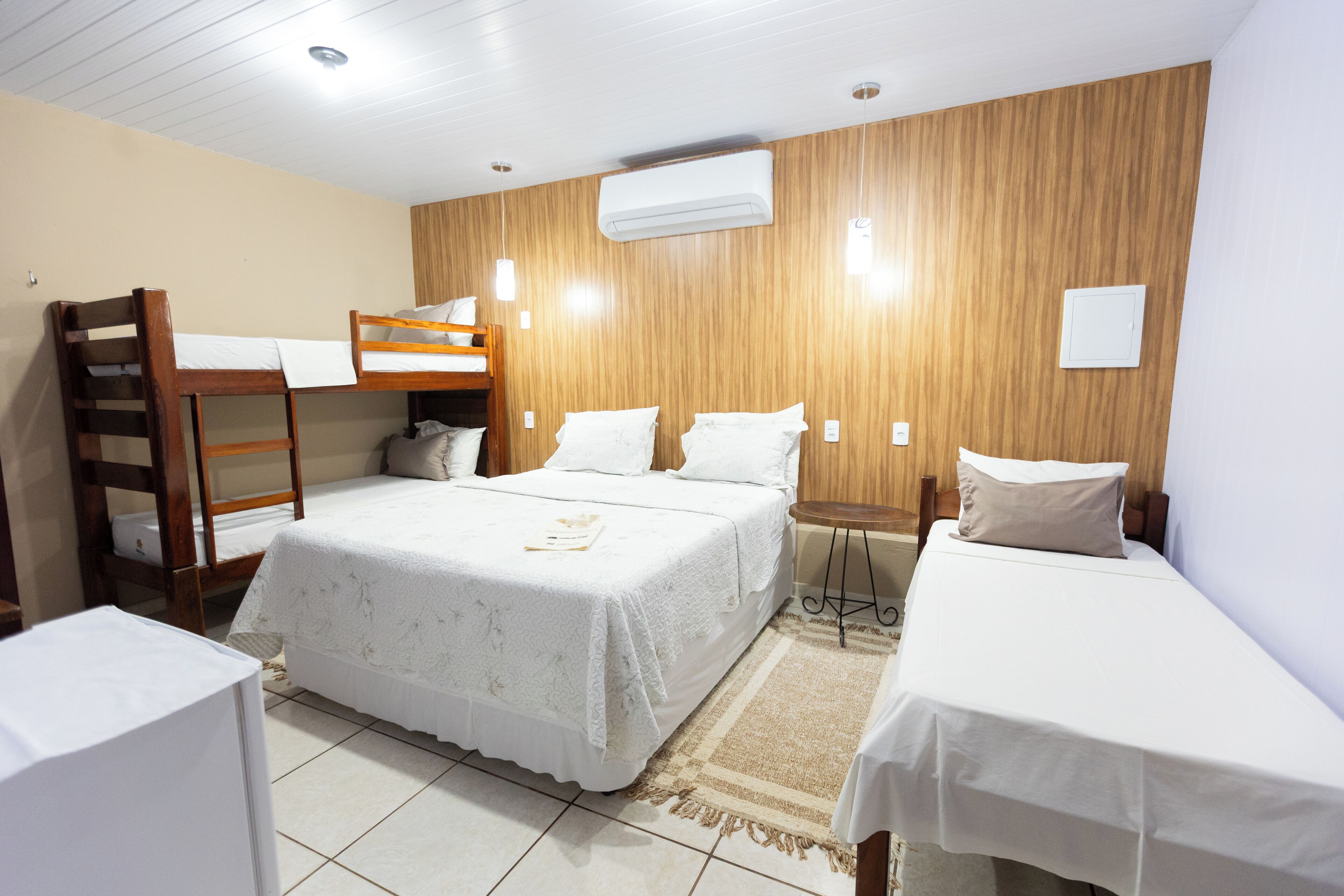 Un dormitorio con dos camas individuales, una litera, un armario de madera y un equipo de aire acondicionado en la pared.