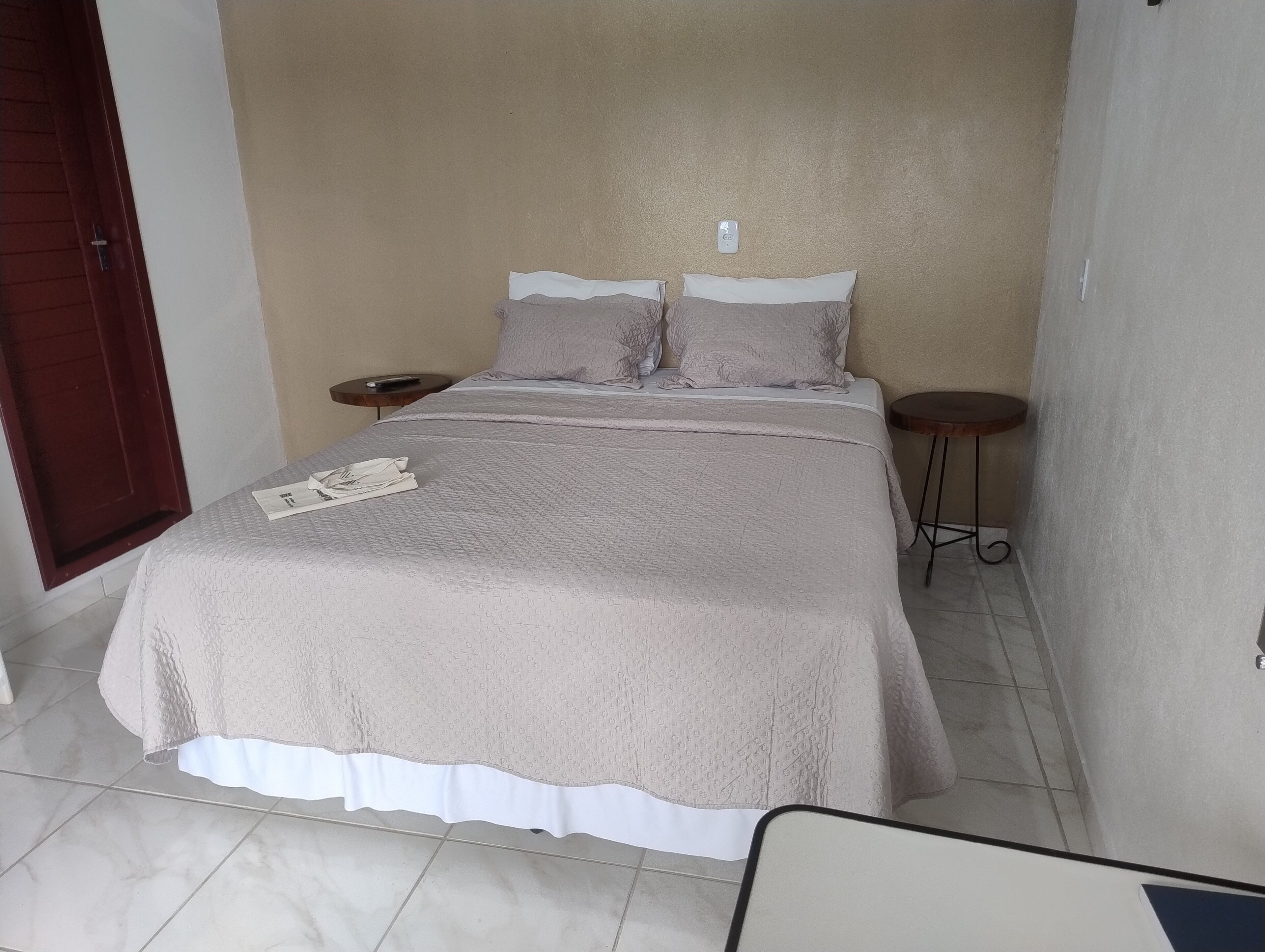 A neatly made bed with a patterned bedspread, two pillows, and a remote control on a bedside table.