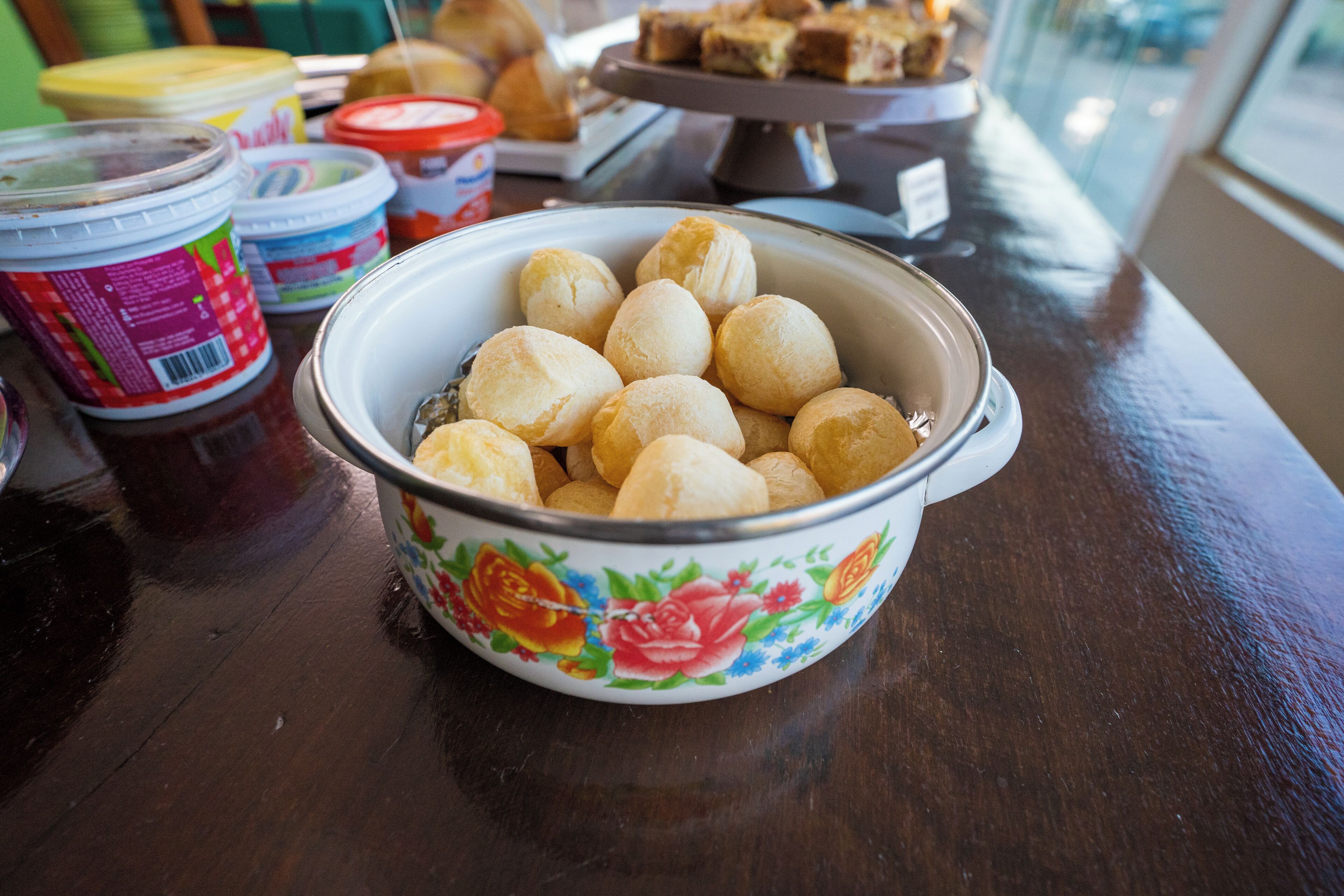 A bowl of round pastries on a wooden table with various food items and containers in the background.