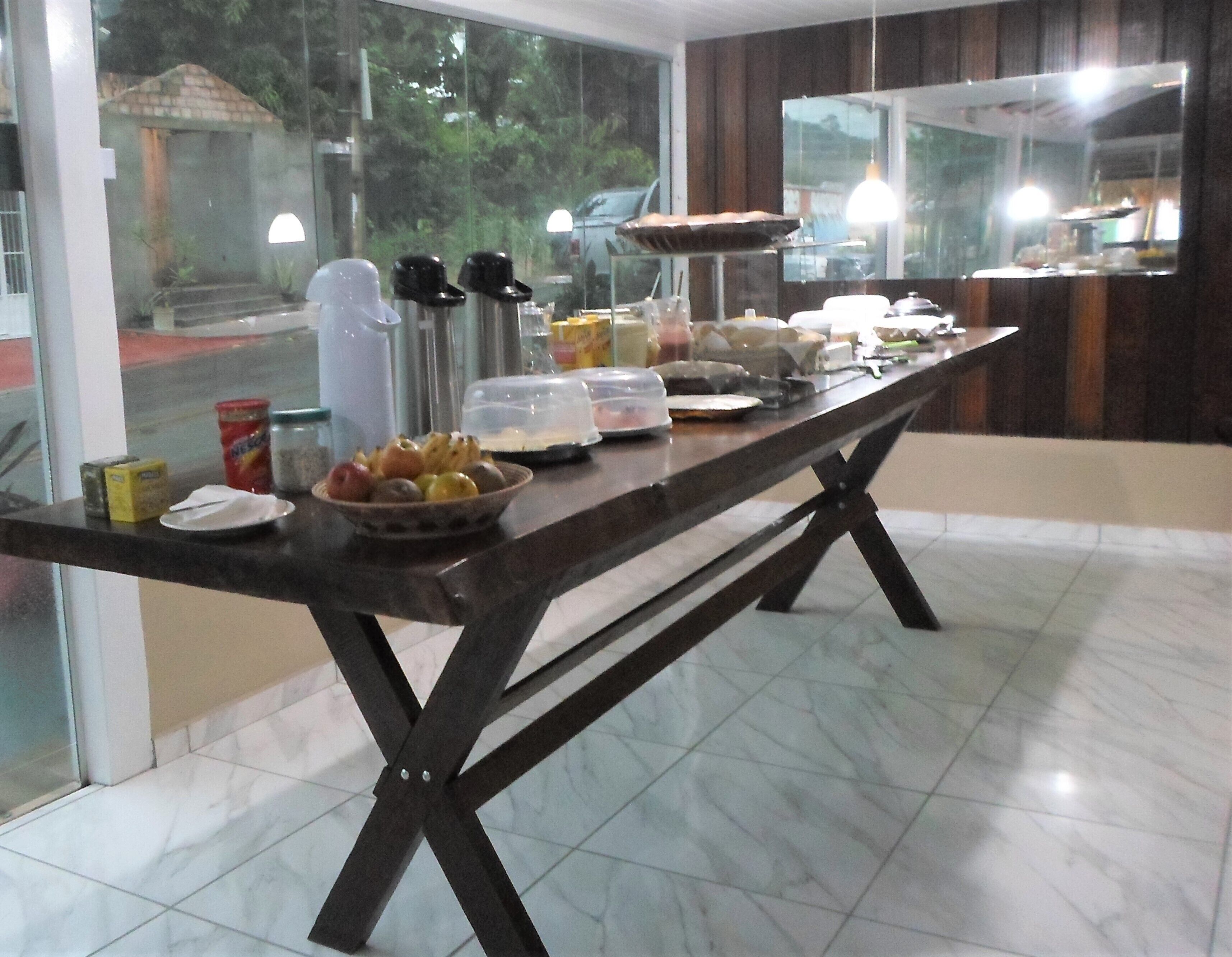 Una mesa de buffet con diferentes alimentos y salsas, ubicada en un espacio con ventanas amplias y piso de baldosas.