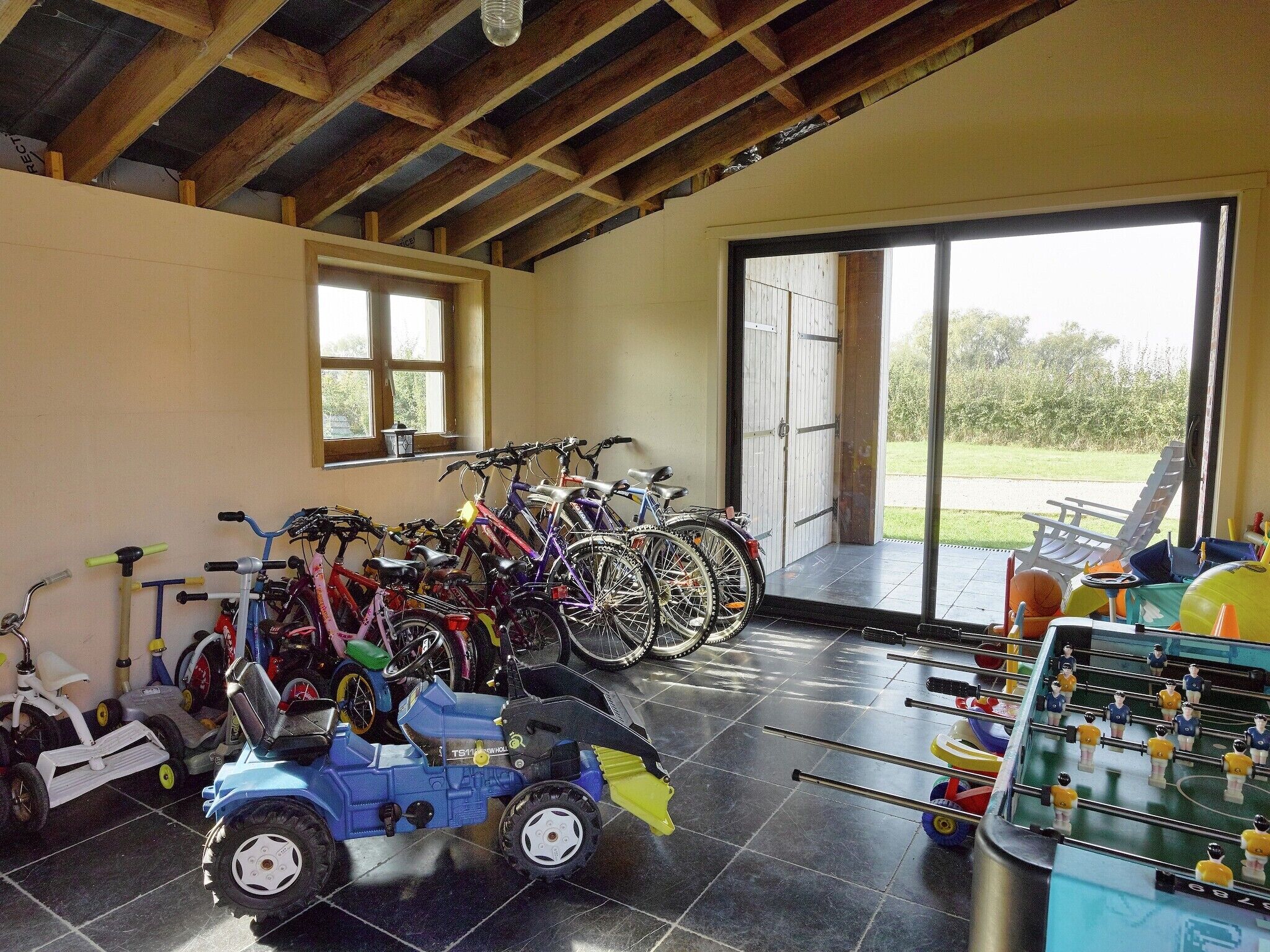 Une pièce où l’on trouve des vélos, un tracteur jouet et une table de baby-foot.