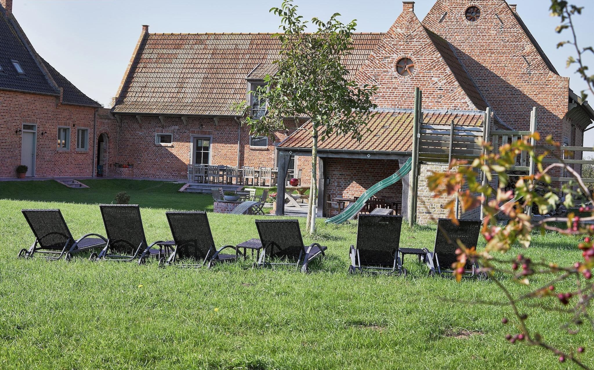 A brick building with a sloped roof, a playground with a slide, and several lounge chairs in the foreground.