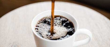 A white cup on a wooden table with coffee being poured into it.