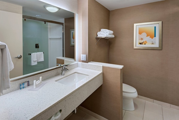 Un baño con dos lavamanos, un inodoro, cabina de ducha de vidrio y un cuadro en la pared.