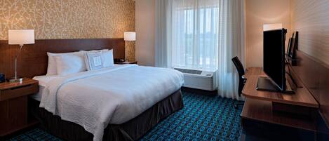 Hotelkamer met een groot bed, een bureau met een flatscreen televisie, een bureaulamp en een raam met gordijnen.