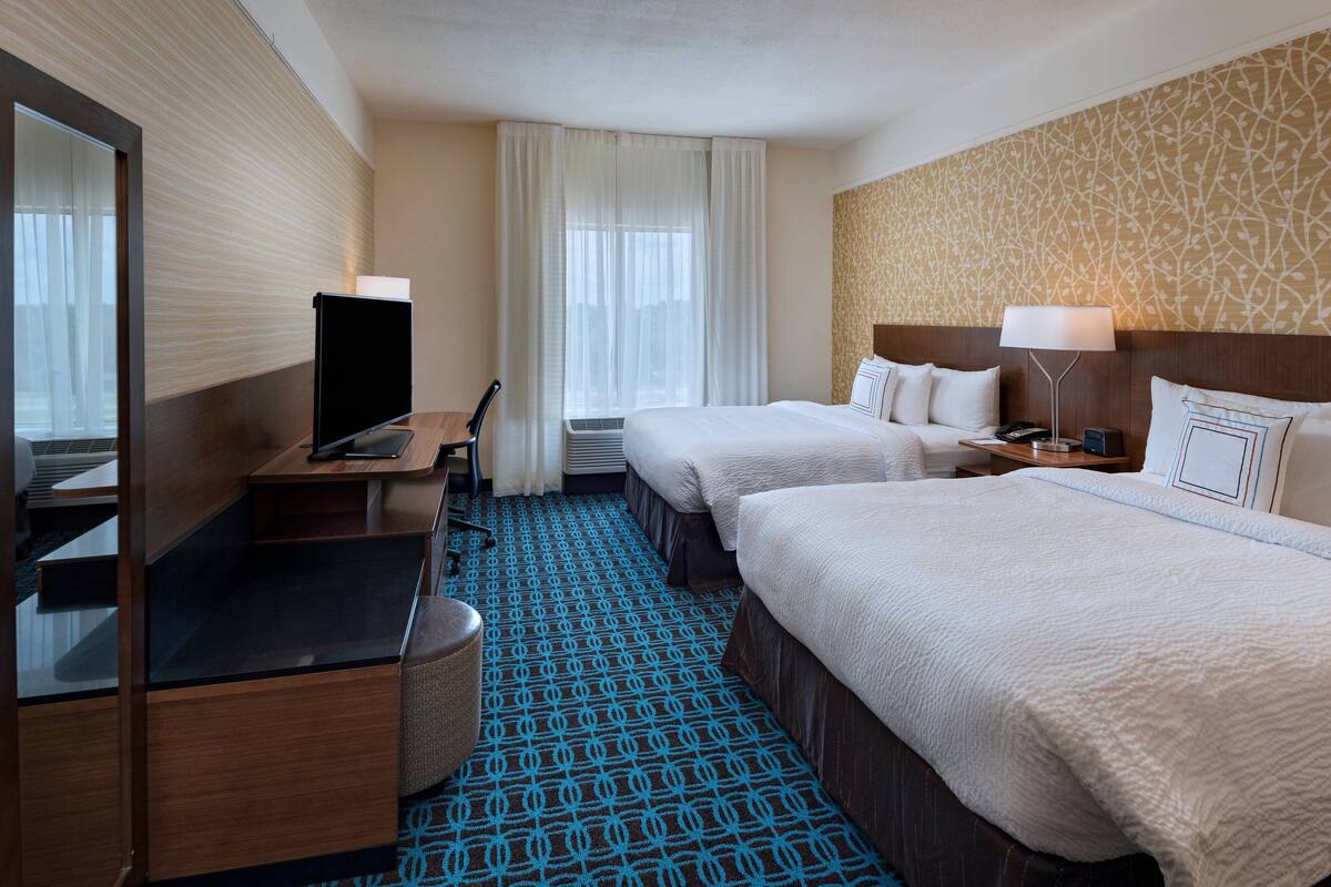 A hotel room with two beds, a desk with a TV, a chair, and a trash bin.
