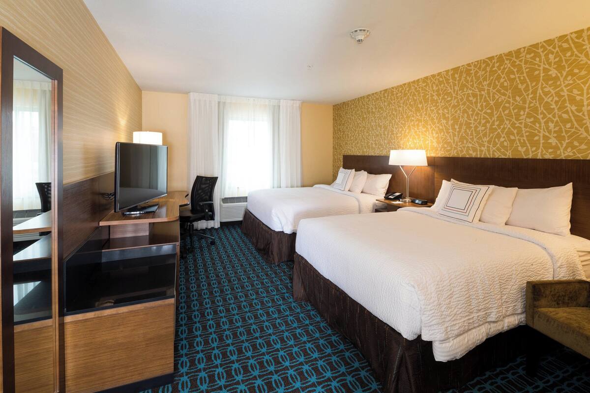 Hotellihuone, jossa on kaksi sänkyä, televisio, työpöytä ja tuoli.
