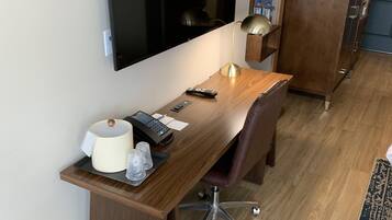 Una habitación de hotel moderna con un escritorio de madera, un televisor de pantalla plana montado en la pared, una lámpara de escritorio y un armario grande.