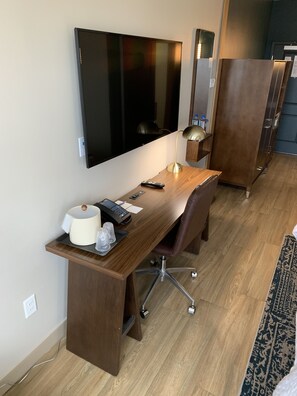 Una camera d'albergo moderna con una scrivania in legno, una TV a schermo piatto montata a parete, una lampada da scrivania e un ampio armadio.