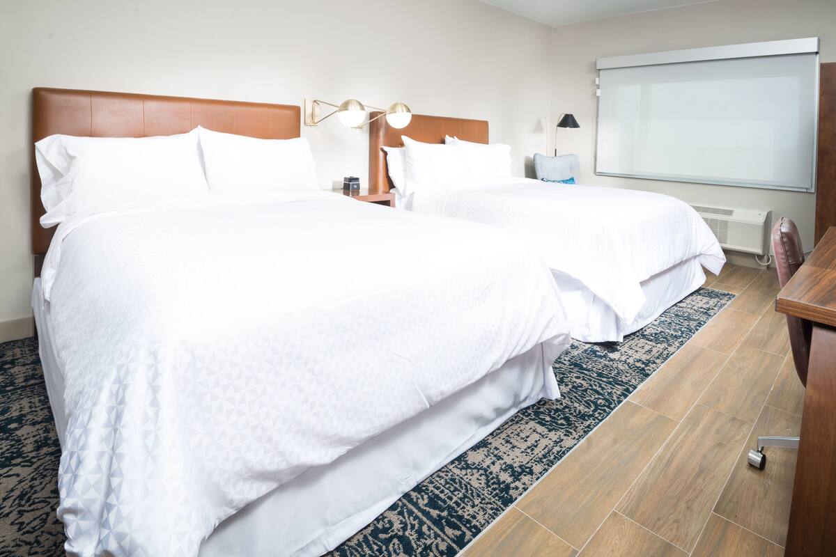 Een hotelkamer met twee bedden, een houten hoofdeinde, een groot raam en een projectiescherm.