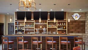 A bar area with wooden chairs and a bar counter. There are shelves with bottles and glasses. A clock is on the wall. - Four Points by Sheraton Houston Intercontinental Airport (Houston)