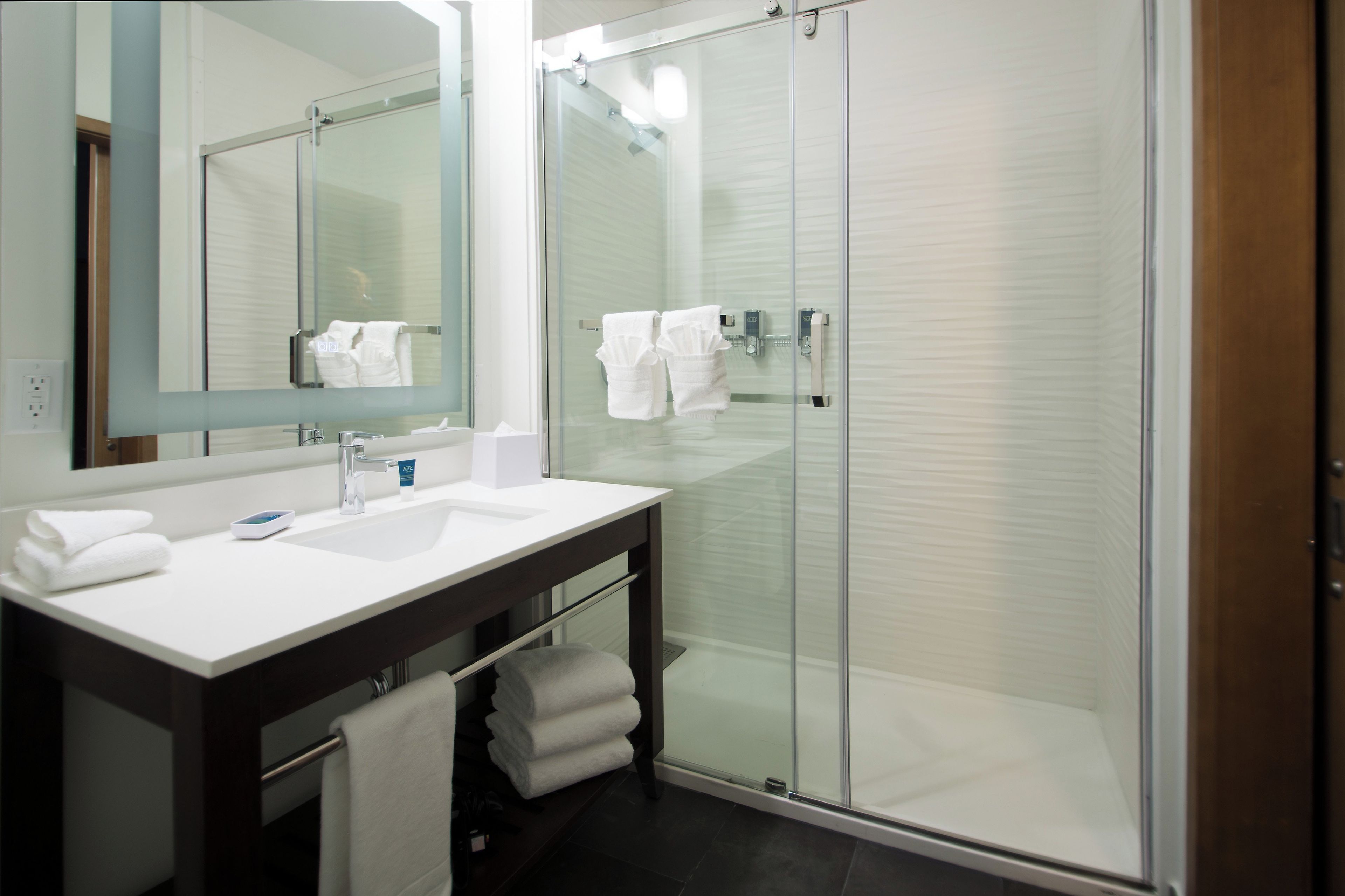 Un baño moderno con cabina de ducha de vidrio, un lavabo blanco y un espejo grande.