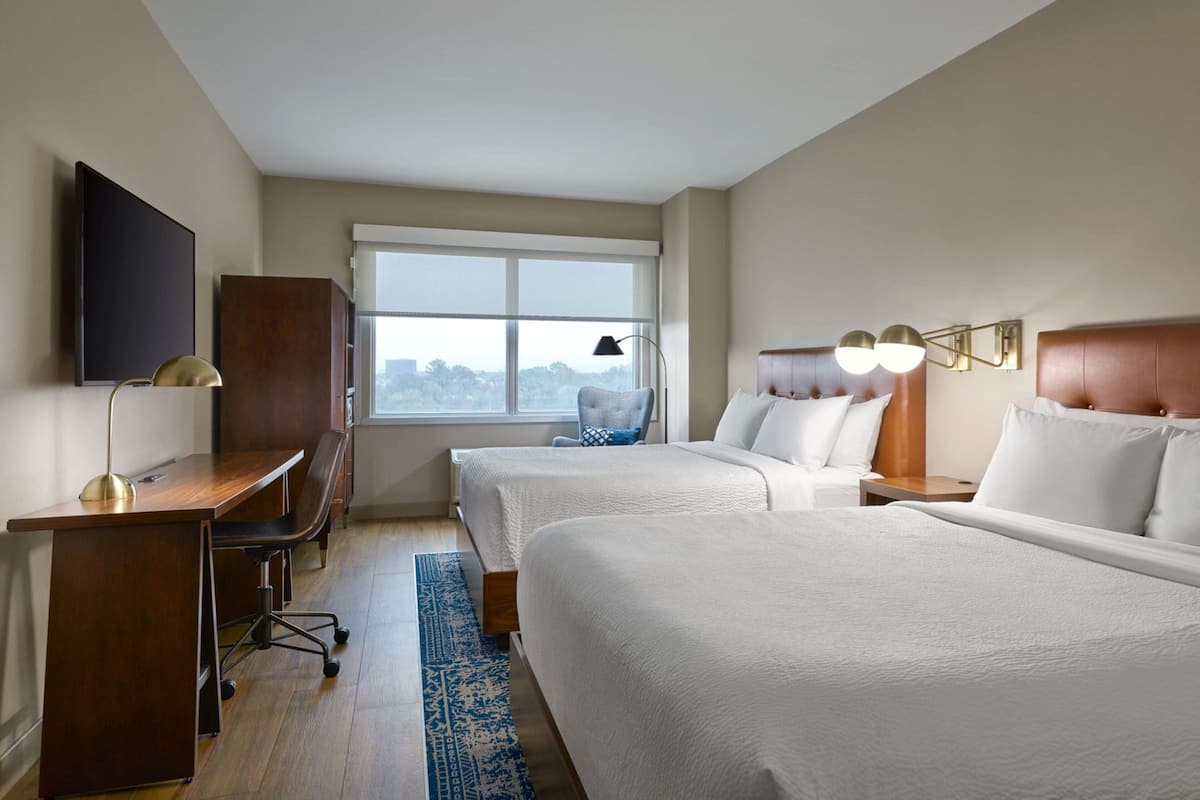 Een hotelkamer met twee bedden, een bureau, een stoel, een televisie en een raam met uitzicht.