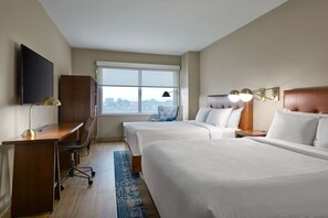 Een hotelkamer met twee bedden, een bureau, een stoel, een televisie en een raam met uitzicht.