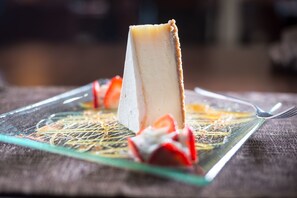 Una fetta di cheesecake su un piatto di vetro con base a griglia, servita con fragole e una forchetta.