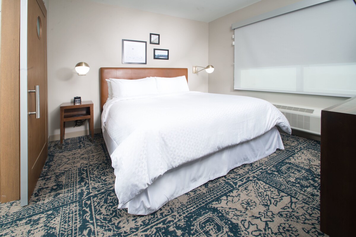 Una camera d'albergo con un letto grande, un comodino con una lampada e una finestra con tende.