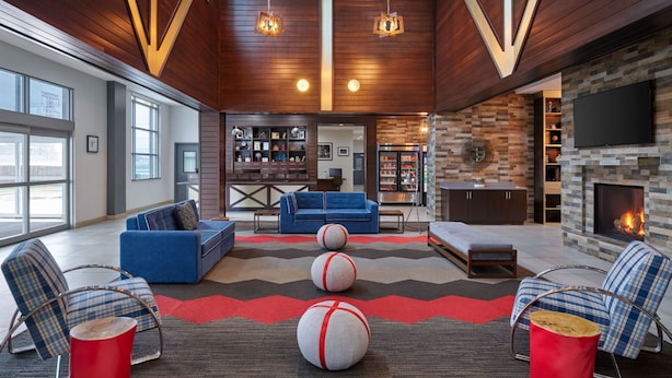 A modern living room with a fireplace, blue sofas, and a red accent wall. - Four Points by Sheraton Houston Intercontinental Airport (Houston)